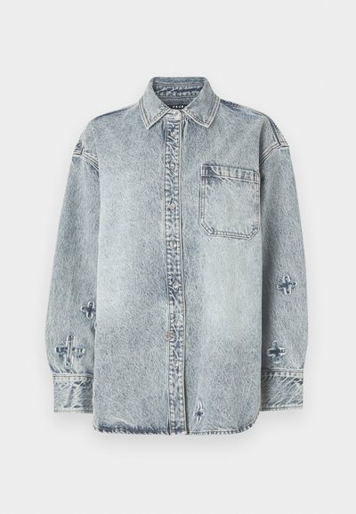 Šviesiai mėlyna džinsinė marškinė su ilgomis rankovėmis, sagų uždarymu, viena krūtinės kišenė ir kryžminiai siuvinėjimai ant rankovių.