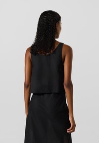 Juodas trumpas tankų viršus su apvaliu kaklu ir plačiomis petnešėlėmis. Pagamintas iš lygaus audinio, su švariu kraštu. Paprastas, minimalistinis dizainas.