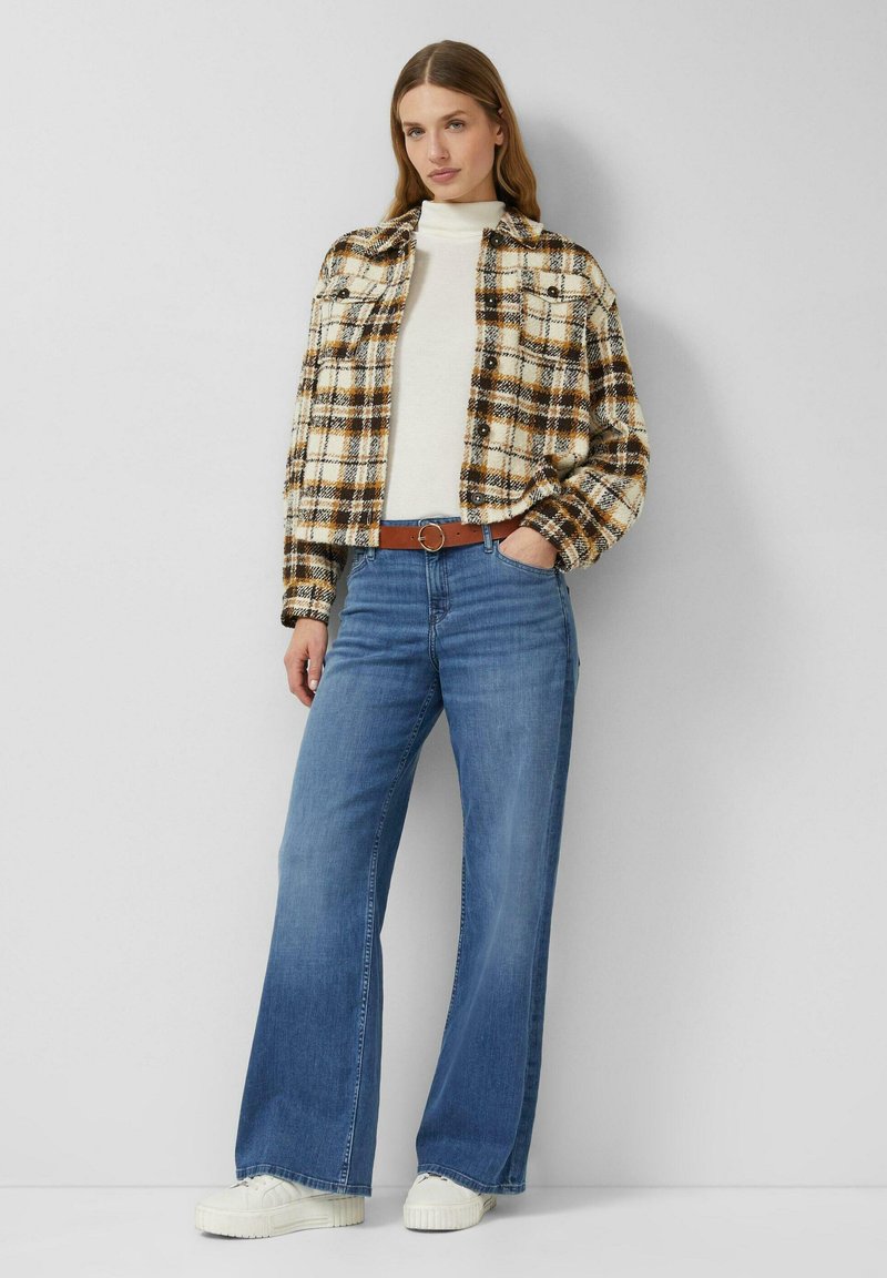 Kurtka w kratę w kolorach kremowym, brązowym i czarnym; biały golf; niebieskie jeansy z szerokimi nogawkami; brązowy pasek; białe trampki. Gładka faktura, styl codzienny.