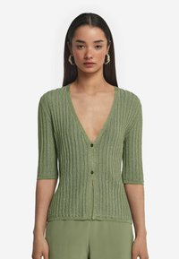 Grön ribbad cardigan med djup V-ringning, korta ärmar och knappar framtill. Tyget har en subtil lyster och en texturerad mönster.