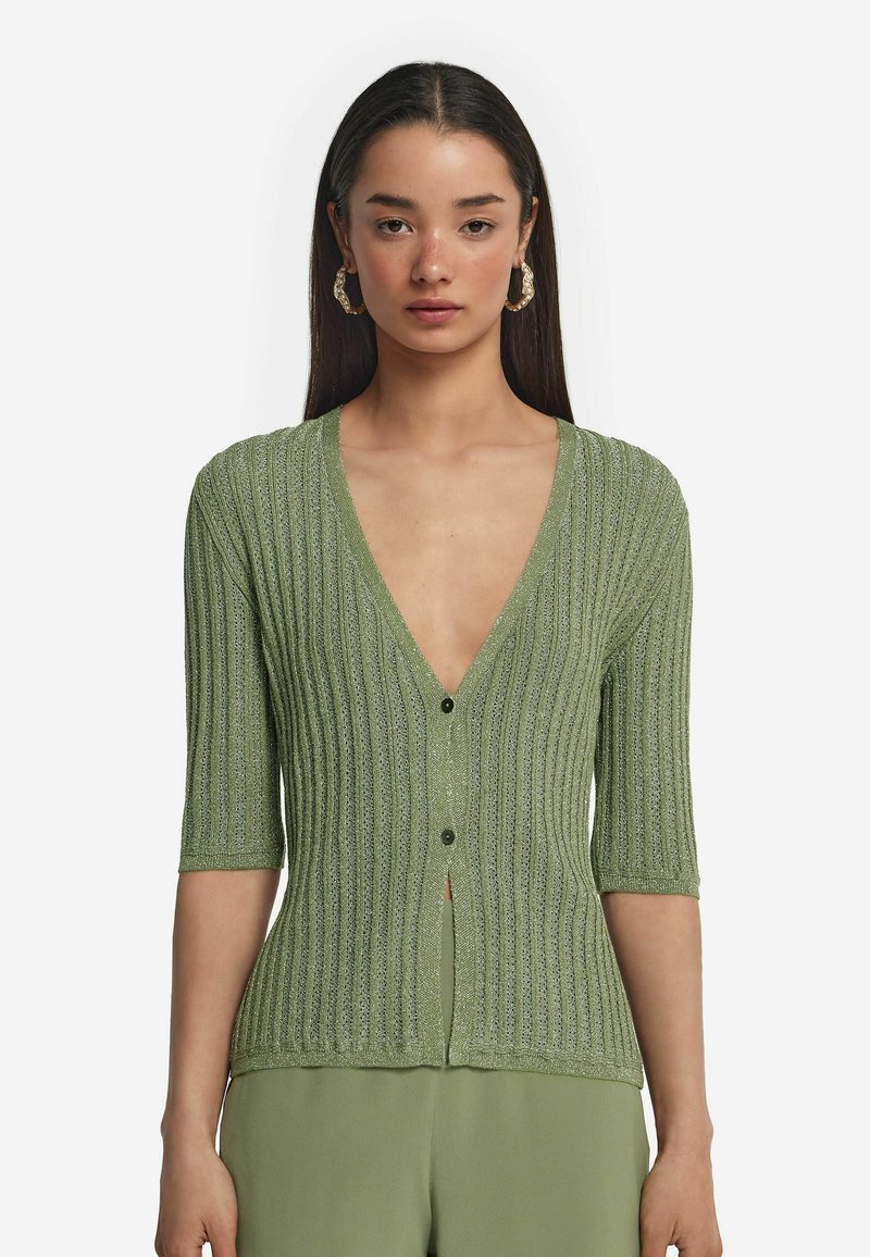 Grön ribbad cardigan med djup V-ringning, korta ärmar och knappar framtill. Tyget har en subtil lyster och en texturerad mönster.