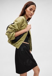Olijfgroene bomberjack, zwart getailleerd topje en zwarte rok met bloemenborduursel. Voorzien van pofmouwen en ritssluiting op de jas.
