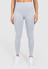 Leggings gris claro con una textura acanalada, cintura alta y un ajuste ceñido. Combinados con zapatillas deportivas blancas con detalles en negro.