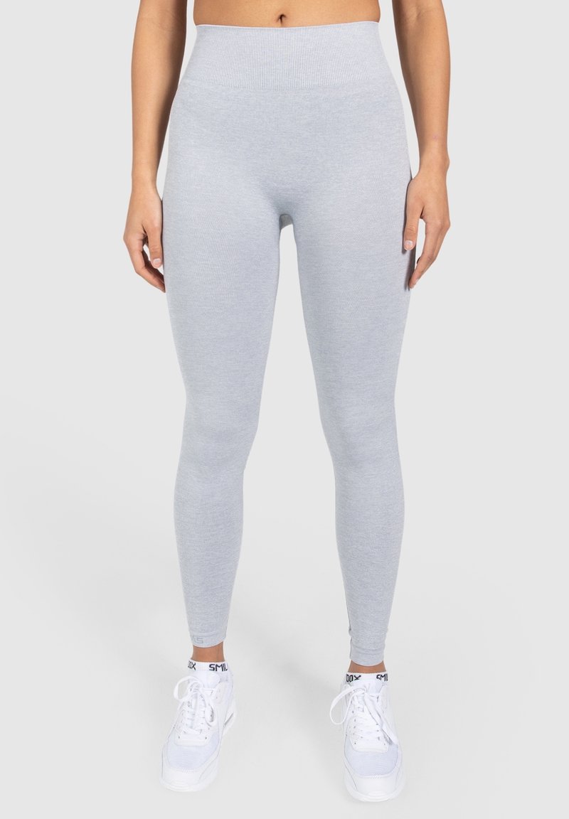 Leggings gris claro con una textura acanalada, cintura alta y un ajuste ceñido. Combinados con zapatillas deportivas blancas con detalles en negro.
