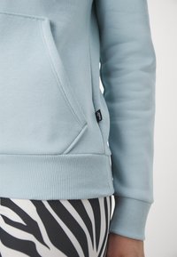 Ljusblå sweatshirt med en känguruficka och ribbade muddar, kombinerad med svarta och vita leggings med zebramönster.