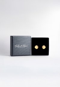 Boucles d'oreilles en or en forme de coquillage dans une boîte d'affichage en velours noir, présentant un design texturé. La boîte a un extérieur lisse et sombre avec un texte embossé.