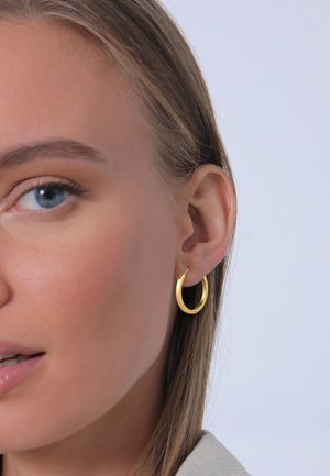 Goldene Creole angezeigt, mit einem glatten, runden Design und einem dünnen Profil. Das Material hat eine glänzende Oberfläche und einen sicheren Verschluss.