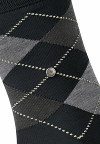 Skarpetka w wzór argyle w odcieniach czerni i szarości z kontrastującym białym szwem oraz małym metalicznym logo. Gładka faktura materiału, standardowy kształt skarpetki.