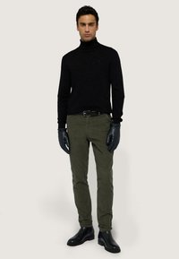 Svart höghalssvett, olivgröna byxor, läderhandskar och svarta ankelstövlar. Slim fit, minimalistik design.