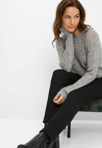 Maglione grigio a maglia con una vestibilità rilassata, maniche lunghe e polsini a coste. Abbinato a pantaloni neri aderenti e stivaletti neri alla caviglia.