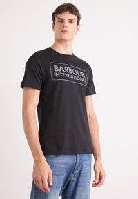 Tricou din bumbac negru, cu un mare logo gri "BARBOUR INTERNATIONAL" pe față. Croiala clasică, cu mâneci scurte și guler rotund.