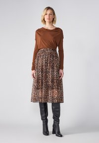 Hnědý dlouhý rukáv s draped výstřihem, kombinovaný s průhlednou sukní s leopardím vzorem. Černé kozačky na vysokém podpatku do kolen.