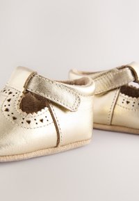 Chaussures pour bébé en cuir doré métallisé, avec un motif découpé en forme de festons, une bride Velcro et une semelle en suède souple.