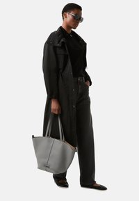 Gray leather tote bag with a textured finish, featuring two long handles and a smooth, contrasting interior, paired with a black outerwear ensemble.