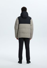 Puffjakke med en beige underdel og en sort overdel med hætte. Designet har en quiltet struktur og polstret isolering.