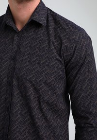 Camicetta scura a fantasia con un sottile design geometrico, caratterizzata da una chiusura con bottoni, maniche lunghe e un colletto classico.