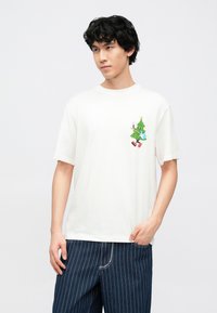 Bijela pamučna majica kratkih rukava s opuštenim krojem i šarenim, crtanim dizajnom božićnog drvca s naglascima.