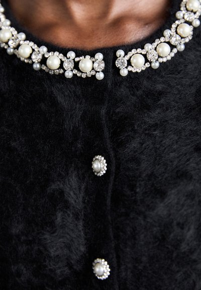 Schwarze Strickjacke aus strukturiertem Stoff, verziert mit einem dekorativen Kragen aus Perlen und Strass sowie passenden Knöpfen.