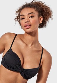 Top de bikini negro con un diseño de frente retorcido, tirantes finos, textura suave y una forma estructurada que proporciona un ajuste de soporte.