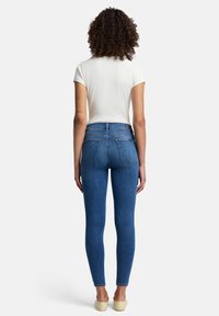 Tunna blå denimjeans med hög midja, två bakfickor och en slät textur. Matchas med en figurnära vit t-shirt.