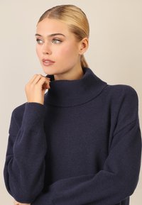 Granatowy sweter z golfem wykonany z miękkiej dzianiny. Posiada szeroki kołnierz, długie rękawy i luźny fason. Gładka faktura z prążkowanymi akcentami.