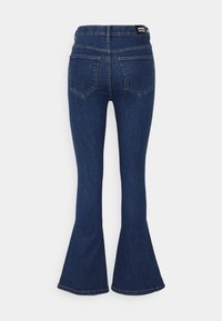 Tummansiniset farkut, joissa on korkea vyötärö ja levenevät lahkeet. Farkuissa on kaksi takataskua ja musta merkkilogo vyötärönauhassa.