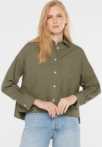 Olive green button-up shirt, long sleeves, chest pocket, soft cotton fabric, relaxed fit, paired with light blue jeans.