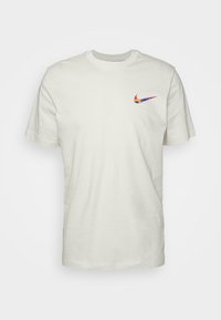 Ljusbeige bomulls-T-shirt med korta ärmar. Har en flerfärgad Nike-logotyp på vänster bröst. Klassisk rundhalsad design.