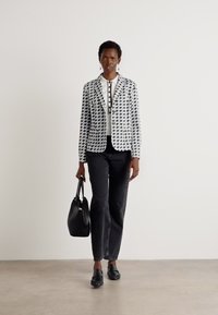 Blazer a strisce in bianco e nero sopra una maglietta bianca, abbinato a pantaloni neri e mocassini. Borsa nera con tracolle.