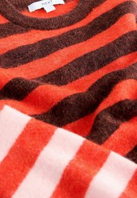 Sarkanais un brūnais svītrotais džemperis ar apaļu kaklu, izgatavots no mīkstas, teksturētas auduma. Redzama etiķete ar uzrakstu "NEXT". Iekļauts balts un rozā svītrots posms.