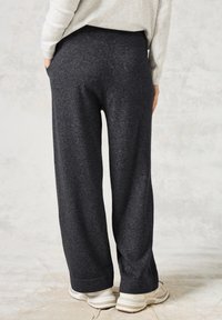 Pantalones de pierna ancha en gris carbón, hechos de una tela suave y texturizada, con bolsillos laterales y un corte cómodo, combinados con zapatillas de color claro.