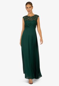 Langes grünes Kleid mit einer Spitzenoberteil und transparentem Überzug. Das Kleid hat eine taillierte Taille und Kappärmel, die eine elegante Silhouette schaffen.