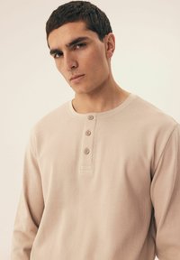 Beżowa, d�ługosleeve'owa koszulka henley z teksturowanej tkaniny, z listwą na trzy guziki i okrągłym dekoltem. Prosty i minimalistyczny design.