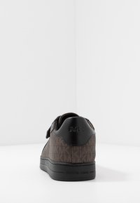 Brun textil-sneaker med ett mönstrat ytskikt, svarta läderdetaljer och en kardborreband. Har en svart gummisula och präglad logotyp.
