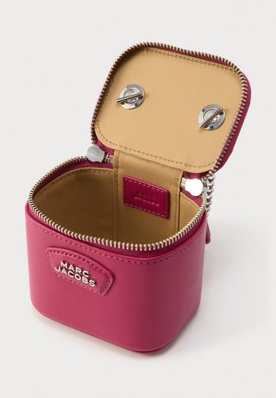 Μικρό ροζ δερμάτινο κουτί με φερμουάρ και ασημένια μεταλλικά στοιχεία· διαθέτει μπεζ εσωτερικό και ετικέτα με το λογότυπο στο εσωτερικό.