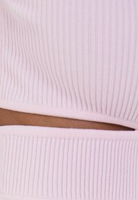 Světle růžový žebrovaný top s přiléhavým střihem a úzkým vykrojením v pase, s jemnou texturou.