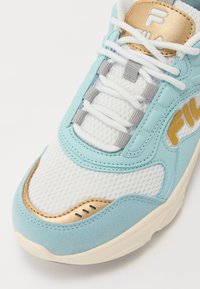 Ljusblå och vit sneakers med överdel i mesh, guldaccenter och texturerad gummisula. Har vita snören och vadderad krage för komfort.