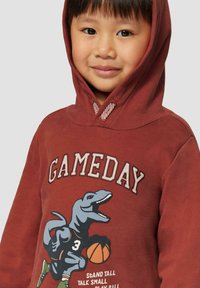 Brązowa bluza z kapturem z grafiką dinozaura, koszykówką oraz napisem "GAMEDAY". Miękka tekstura z ryflowanym kapturem i akcentami.