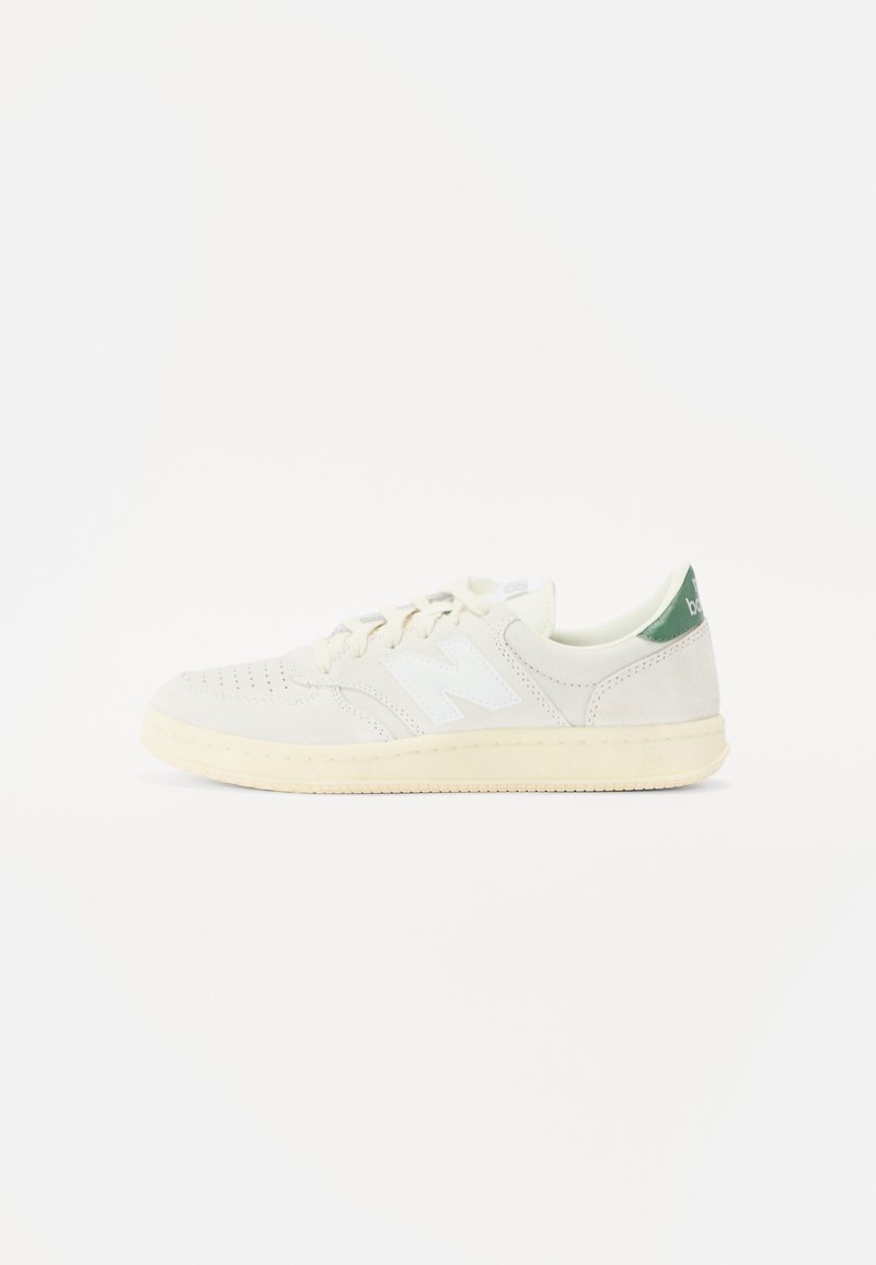 Baskets blanches avec une semelle crème, un bout perforé, des lacets blancs, un logo blanc "N" et une languette de talon verte.