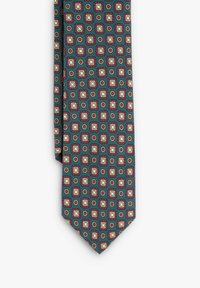 Corbata de seda con fondo verde azulado, que presenta un patrón repetido de cuadrados blancos con borde rojo y pequeños círculos dorados.