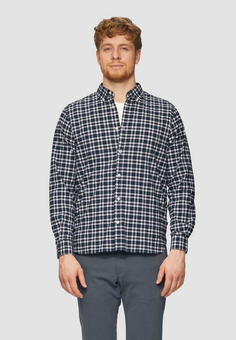 Camicia a quadri blu navy e bianca con colletto aperto, maniche lunghe e vestibilità comoda. Abbinata a pantaloni grigi.