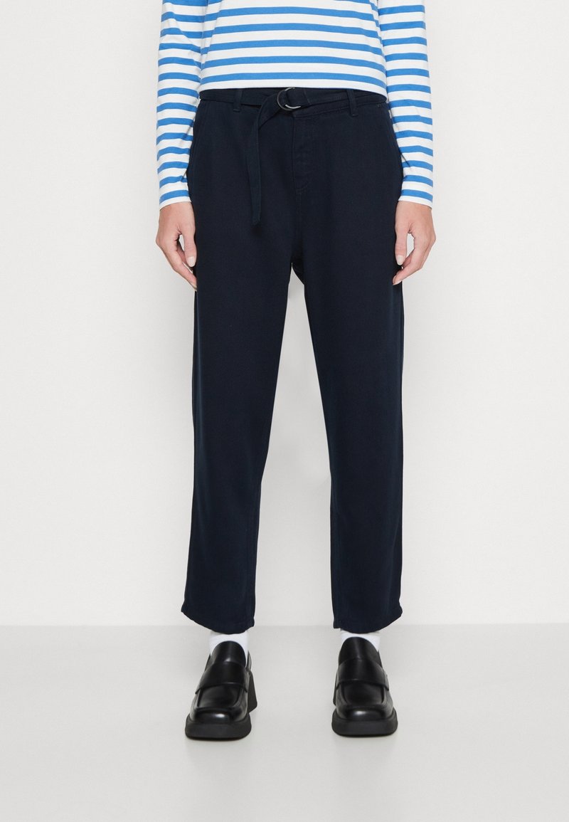 Marelse broek met een riem, aansluitende pasvorm, lichtgewicht stof, met zijzakken en een subtiele textuur. Gepaard met zwarte instappers en witte sokken.