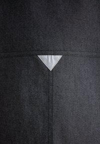 Grey denim fabric with a textured finish. Notable triangular silver accent at the center back. Clean, minimalistic design.