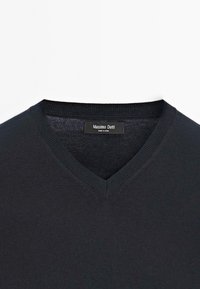 Dunkel schwarzer V-Ausschnitt-Pullover mit geripptem Kragen, aus einem weichen, strukturierten Stoff gefertigt. Mit einem Etikett, das am Halsausschnitt sichtbar ist.