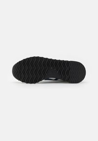 Black rubber shoe sole with a textured pattern featuring deep grooves and a raised logo detail, designed for traction and durability.