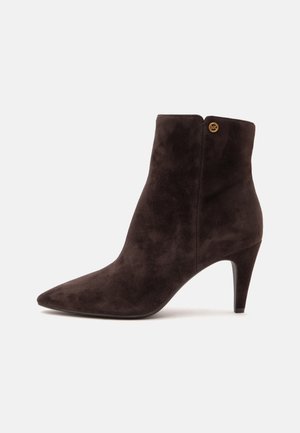 Stivaletto in camoscio marrone scuro con punta appuntita, tacco alto e sottile e piccolo logo dorato vicino al bordo superiore su sfondo uniforme.