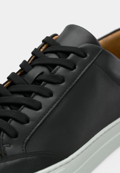 Μαύρα δερμάτινα αθλητικά παπούτσια με λείες επιφάνειες, διαθέτοντας επίπεδα μαύρα κορδόνια και λευκή λαστιχένια σόλα. Κομψός σχεδιασμός με μινιμαλιστικές λεπτομέρειες.