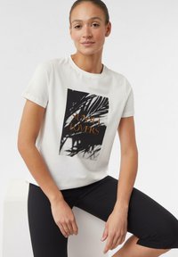 Biała bawełniana koszulka z krótkim rękawem, ozdobiona czarno-białym nadrukiem liścia palmy oraz napisem "SUNSET LOVERS" w złotym kolorze. Okrągły dekolt.