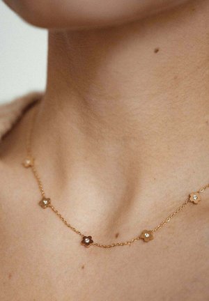 Gold chain necklace featuring alternating flower-shaped links with tiny clear gemstones in the center. Smooth metallic texture.