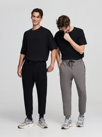 Czarny bawełniany t-shirt o luźnym kroju. Szare spodnie dresowe z elastycznym paskiem w talii, kieszeniami na zamek i ściągaczami przy nogawkach. Oba ubrania noszone ze sportowymi trampkami.